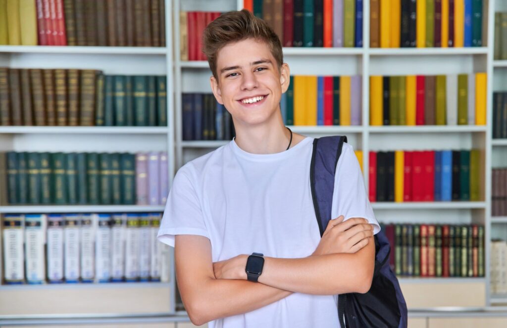 Single portrait of smiling confident male student teenager looking at camera in library